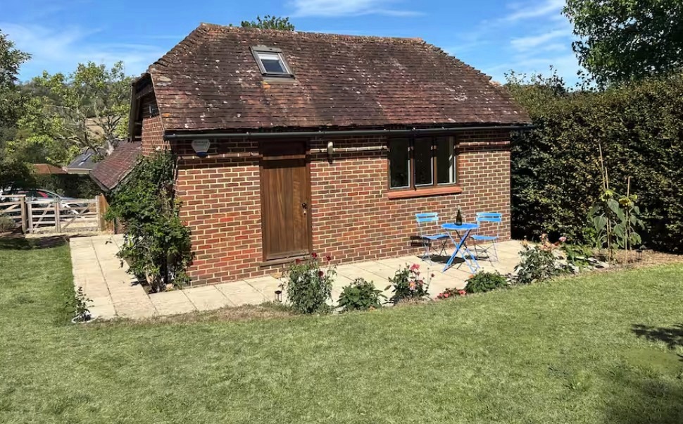 Shere Retreat, a red brick garden annexe with a patio, blue bistro table and chairs, and a lawn in front, under a clear blue sky