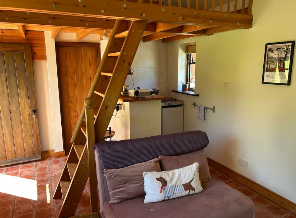 Wooden steps up to the mezzanine bed beside the kitchenette and sofa